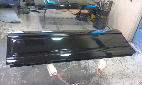 1995 Ford Bronco - A shiny black tailgate sits on the floor of a garage, reflecting the overhead lights.