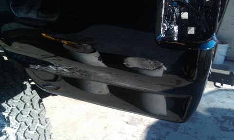 1995 Ford Bronco - Close-up of a black vehicle's rear bumper showing damage, with a portion of an off-road tire visible.