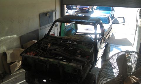 1995 Ford Bronco - A disassembled pickup truck sits in a garage, with other vehicles visible through the open bay door.