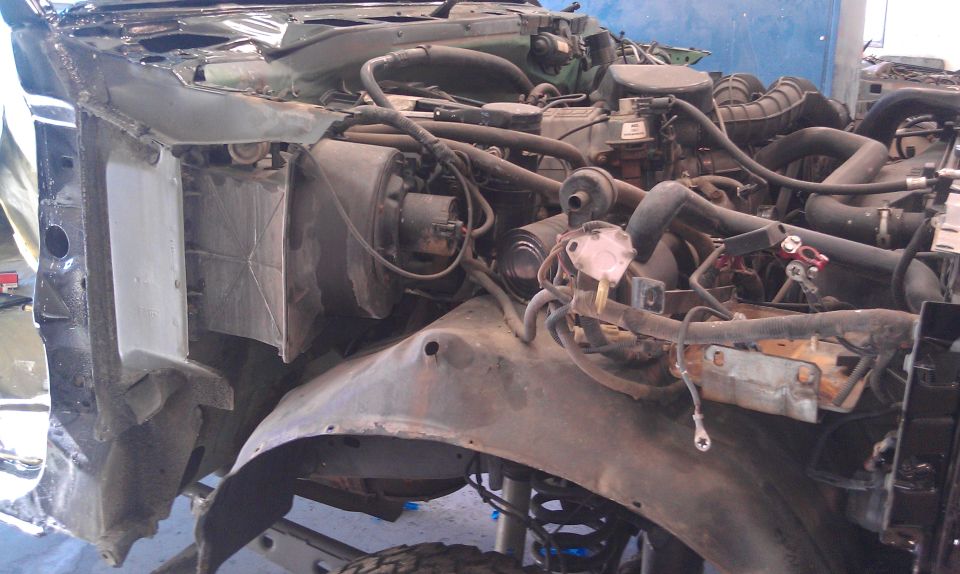 Stripped truck engine bay with fender removed, exposing radiator, brake booster and intake plenum