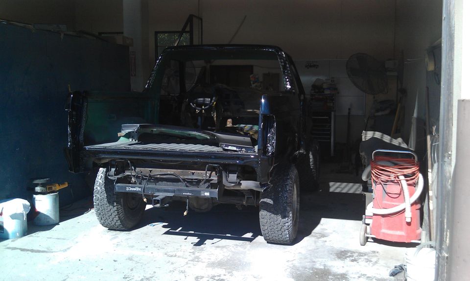 Dark green Ford truck rear three-quarter in garage, no tailgate, mud tires, DrawTite hitch
