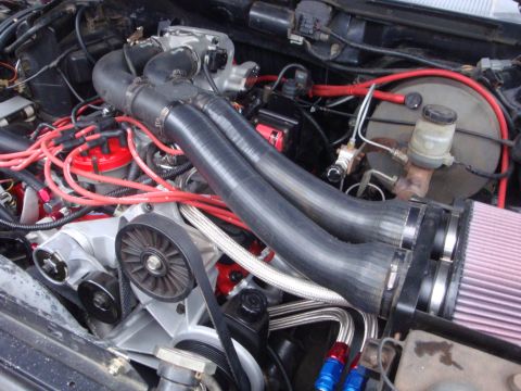 1989 Ford Bronco - Close-up view of a modified engine bay dual intake pipes and prominent red spark plug wires.