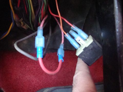 1989 Ford Bronco - A finger points to a black electrical relay connected to a bundle of wires, with red carpeting in the foreground.