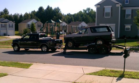 1985 Ford Bronco - A two-tone 1985 Ford Bronco is transported on a trailer towed by a black pickup truck.