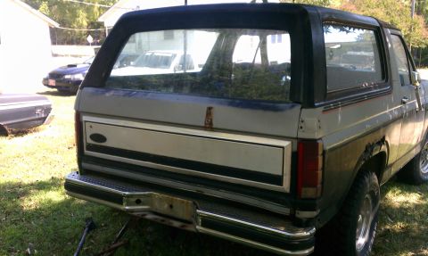 1985 Ford Bronco - The rear of a Ford Bronco shows its tailgate and bumper, with other vehicles in the background.