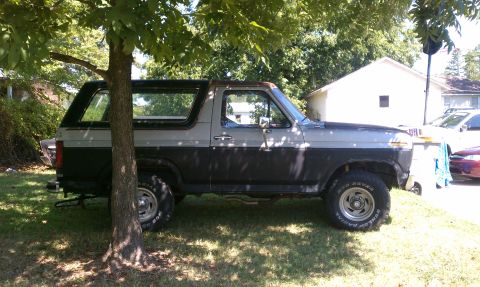 1985 Ford Bronco - This 1985 Ford Bronco, seen from the side, is parked in a grassy area with a tree providing shade.