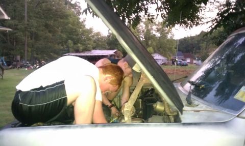 1985 Ford Bronco - Two individuals are actively engaged in maintenance work under the hood of a silver vehicle.