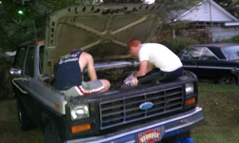 1985 Ford Bronco - Two individuals are attending to the engine of a 1985 Ford Bronco, with another vehicle visible in the background.