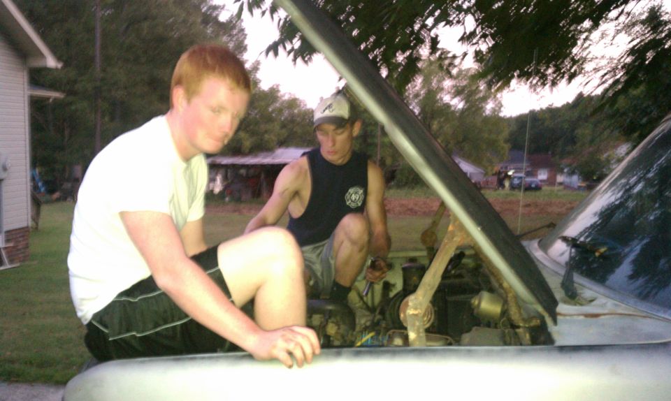 Two men working on the engine of a car with the hood up
