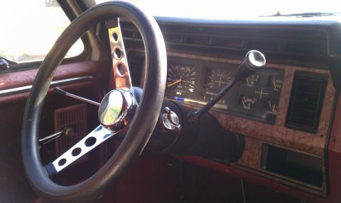 1985 Ford Bronco - The dashboard and steering wheel of an older vehicle are visible, with a floor-mounted shifter.
