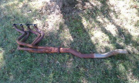 1985 Ford Bronco - Exhaust manifold and pipe lying on grass.