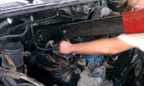 1985 Ford Bronco - A mechanic works on the engine of a vehicle, focusing on the carburetor and surrounding components.