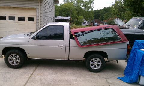 1985 Ford Bronco - Silver Nissan pickup truck with a red camper shell is parked in a driveway.
