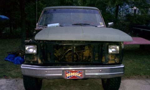 1985 Ford Bronco - This truck, possibly a Ford Bronco, is missing its grille and has its hood open. A "Redneck" license plate is visible on the front bumper.