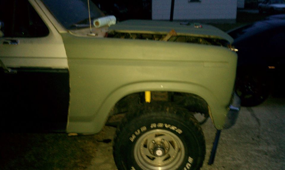 Side view of a green Ford Bronco with the hood open, showing the front fender and part of the door