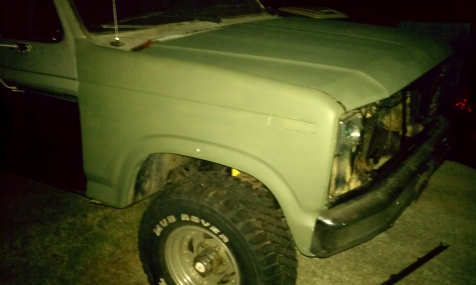 Front fender, headlight area, and tire of a light green Ford Bronco. The grille is missing