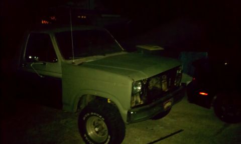 1985 Ford Bronco - A green pickup truck with a damaged front end is parked next to another vehicle.