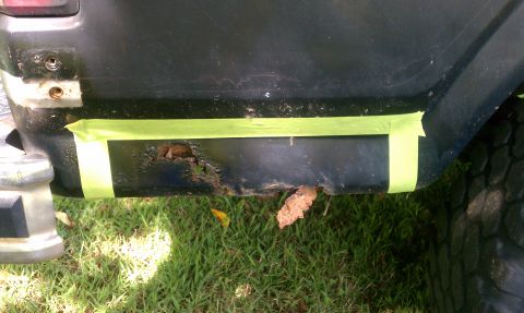1985 Ford Bronco - A rusted section of a vehicle's rear quarter panel is covered with green masking tape.
