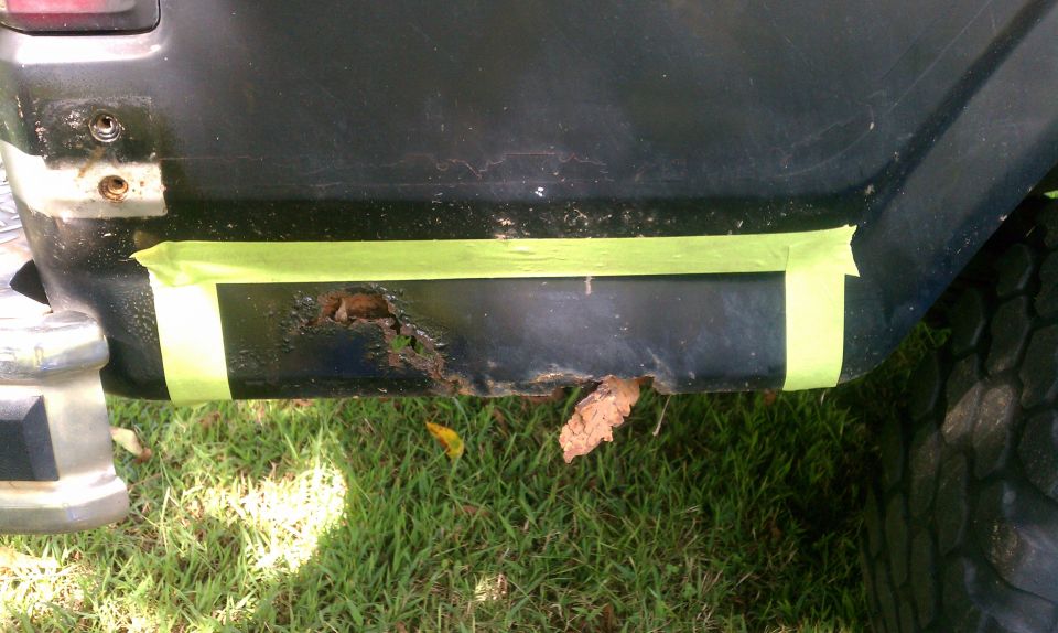 Black vehicle rear quarter panel with rust hole covered by green tape