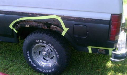 1985 Ford Bronco - This 1985 Ford Bronco shows significant rust damage around the rear wheel well, with yellow tape marking areas for repair.