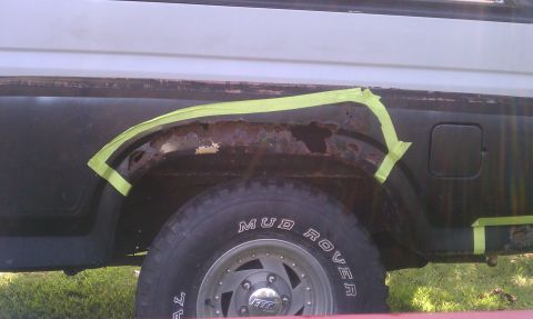 1985 Ford Bronco - The rear wheel well of a vehicle shows significant rust damage, with green tape marking the area for repair.