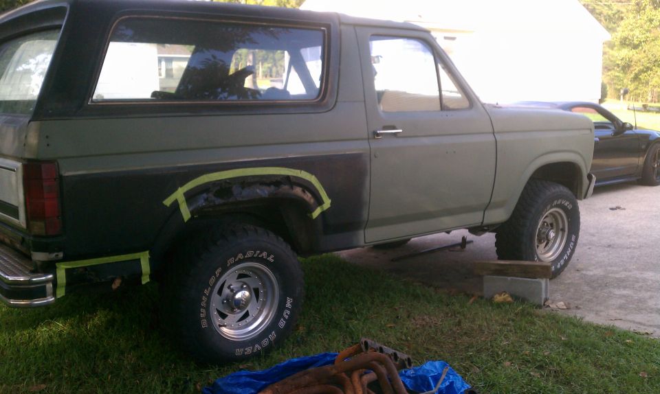 Green Ford Bronco with black rear quarter panel, taped for repair, on grass