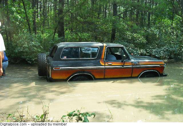 Side view of a 1979 Ford Bronco II stuck in mud, orange and black