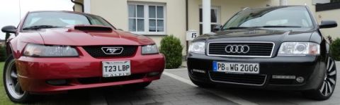 2003 Audi A6 - Two cars, a red Ford Mustang and a black Audi A6, are parked in a driveway in front of a house.