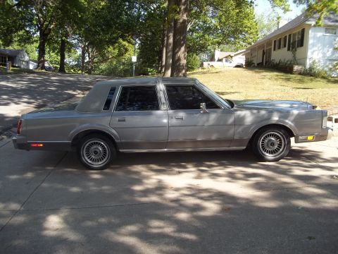 1988 Lincoln Town Car - This 1988 Lincoln Town Car is parked on a paved surface with a house and trees in the background.