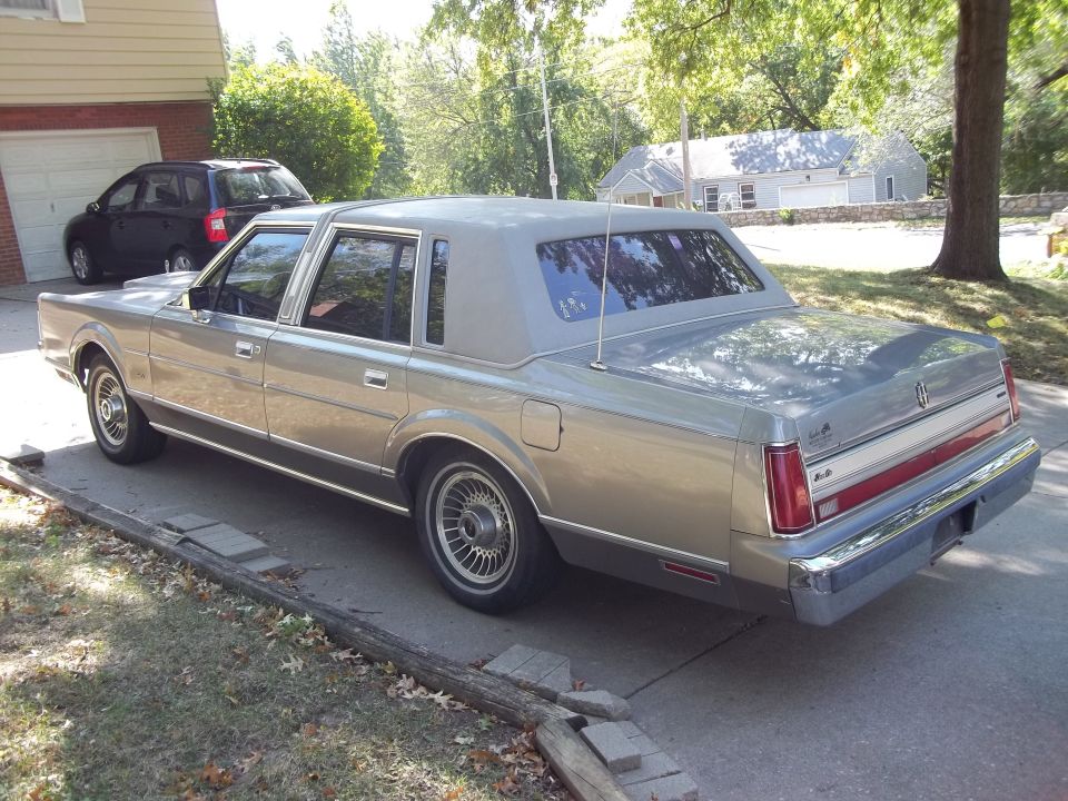 Silver 1988 Lincoln Town Car parked on driveway, rear 3/4 view. Another dark SUV is visible in the garage