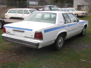 1991 Ford Crown Victoria LTD - Rear three-quarter view of a white 1980s Ford LTD Crown Victoria sedan with blue racing stripes.