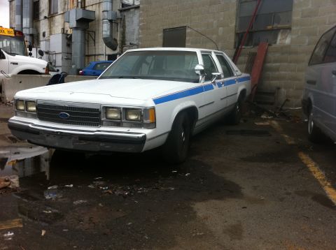 1991 Ford Crown Victoria LTD - A white 1991 Ford Crown Victoria LTD sedan with blue racing stripes is parked outdoors.