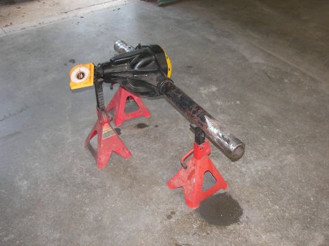 1988 Ford Bronco - A front axle assembly is supported by red jack stands, with a yellow angle finder attached to one end.