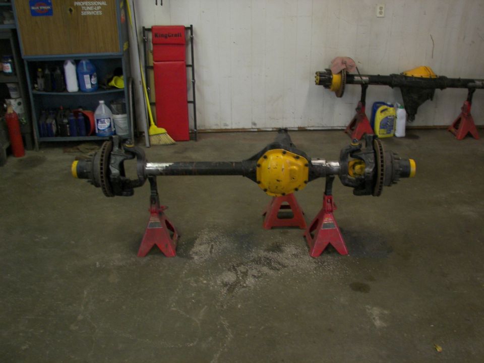 Two vehicle axle assemblies on red jack stands in a garage. One is in the foreground, the other is further back
