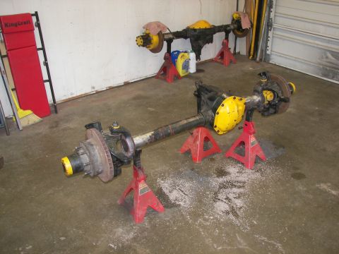 1988 Ford Bronco - Two vehicle axles are supported by red jack stands in a garage setting.