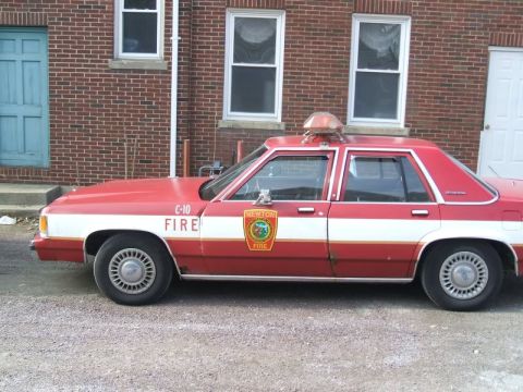1991 Ford Crown Victoria LTD - A side view of a vintage fire department sedan parked in front of a brick building.