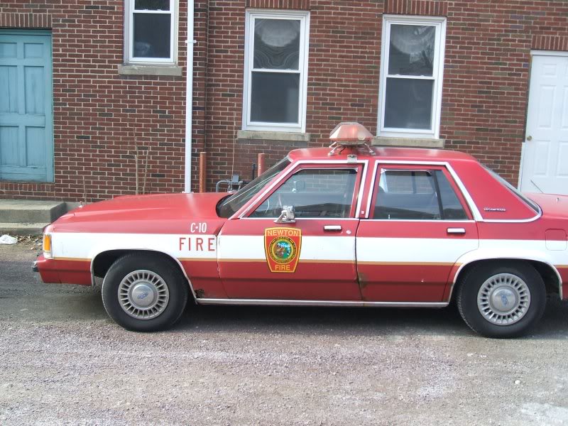 red and white sedan with 'C-10 FIRE' and 'NEWTON FIRE' markings, light bar on roof