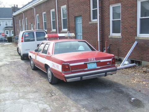 1991 Ford Crown Victoria LTD - A 1991 Ford Crown Victoria LTD police car, marked with 'FIRE' and 'CALL 911', is parked next to a white van.