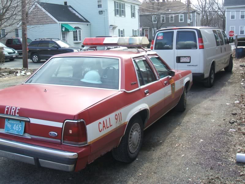 1991 Ford Crown Victoria LTD police car with "FIRE" and "CALL 911" markings, parked next to a white van