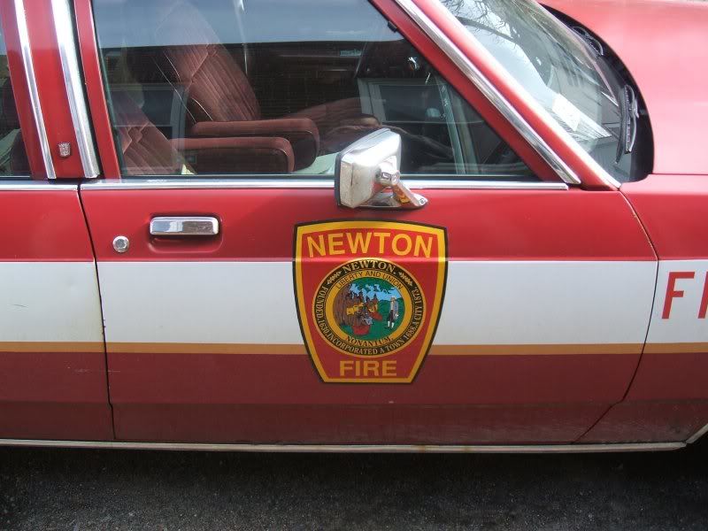 Side view of a red and white emergency vehicle with a Newton Fire Department emblem on the door