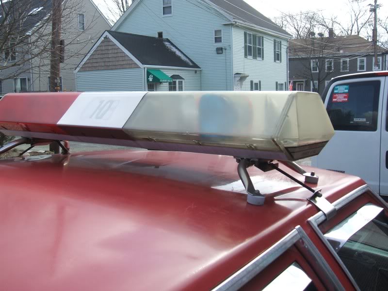 Red vehicle roof with emergency light bar, white van visible