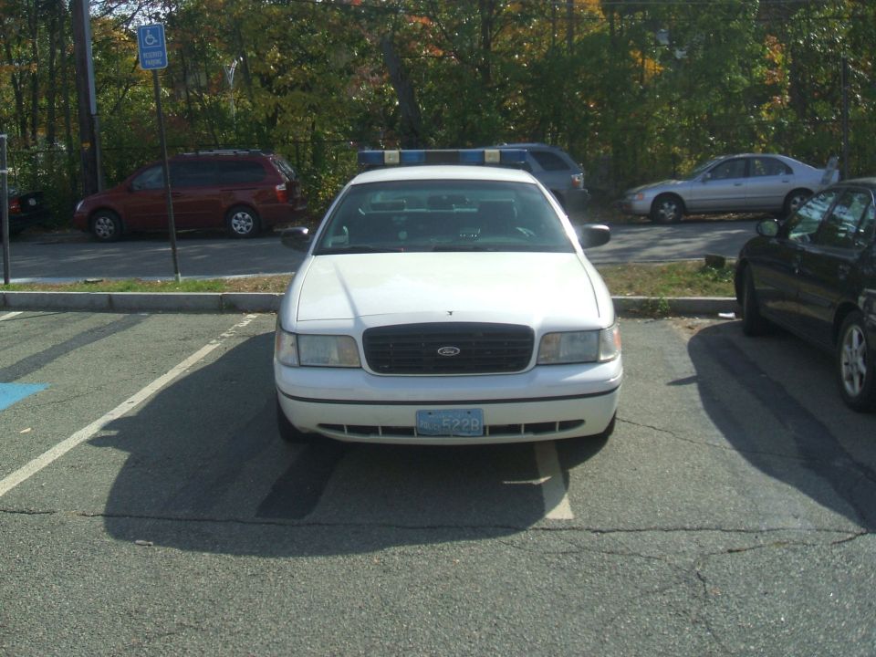 White Ford Crown Victoria police car parked in a lot, blue light bar on top
