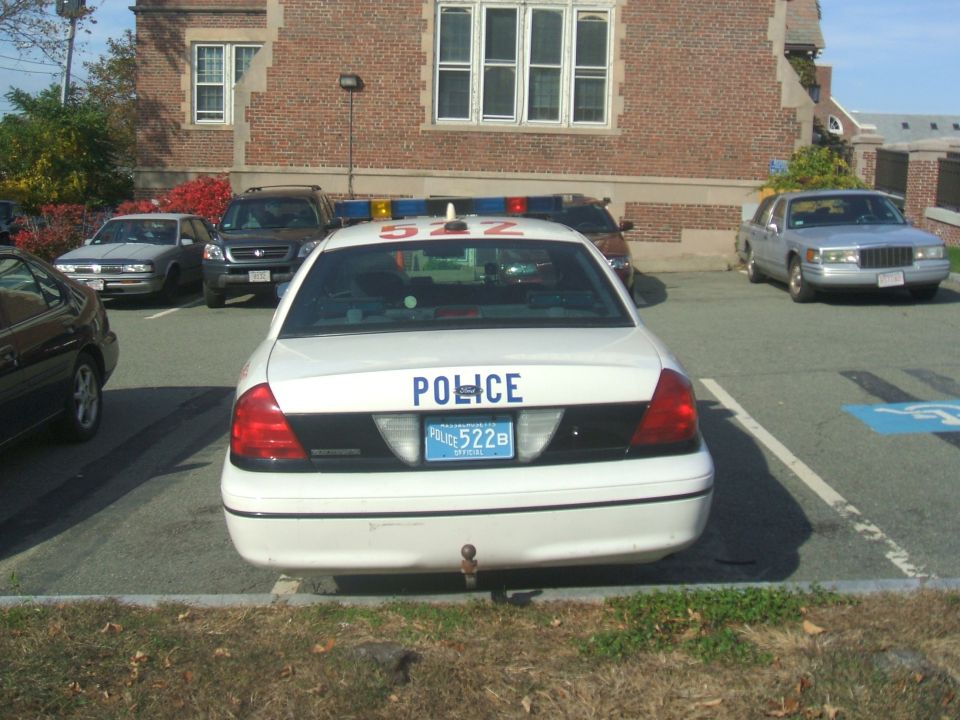 Rear view of a white police car with 'POLICE' and '522B' visible on the trunk, parked next to other vehicles