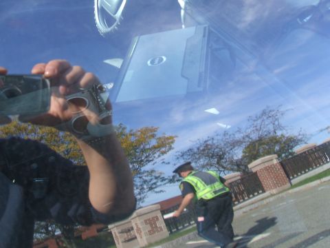 1991 Ford Crown Victoria LTD - A police officer and a laptop are reflected in the windshield of a vehicle on a sunny day.