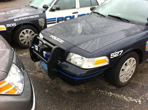 1991 Ford Crown Victoria LTD - Two police cars are parked close together on a wet surface. The car in the foreground has "POLICE" written on its hood and the number 527 o…
