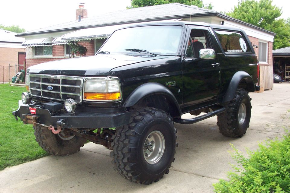 Black lifted Ford Bronco SUV on large off-road tires with front winch in a driveway.