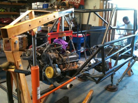 1966 Ford Bronco - A custom chassis frame is being worked on in a garage with an engine suspended above it.