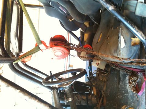 1966 Ford Bronco - Interior view of a vehicle showing worn seats and a steering wheel, with a chain hoist overhead.