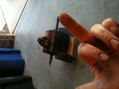 1966 Ford Bronco - A dirty hand points to a rusty steering gearbox on a concrete surface.