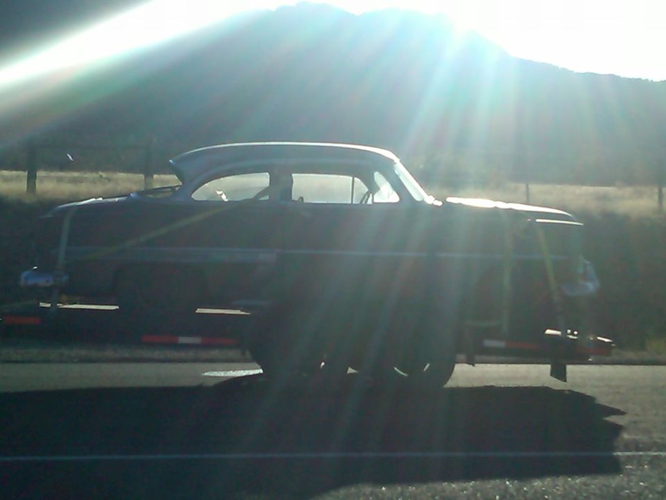 Dark-colored 1953 Chevrolet Bel Air coupe on a trailer, seen from the side in bright sunlight